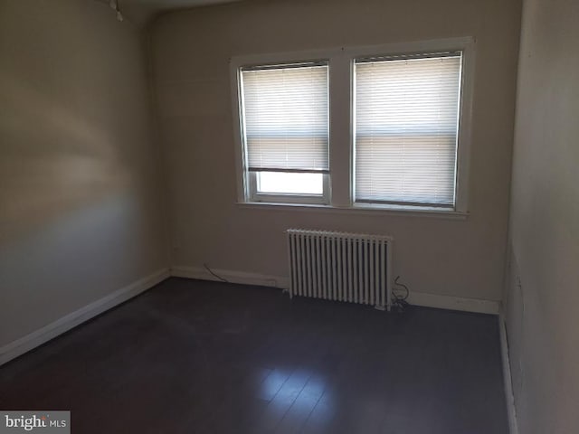 unfurnished room featuring dark wood finished floors, radiator, and baseboards