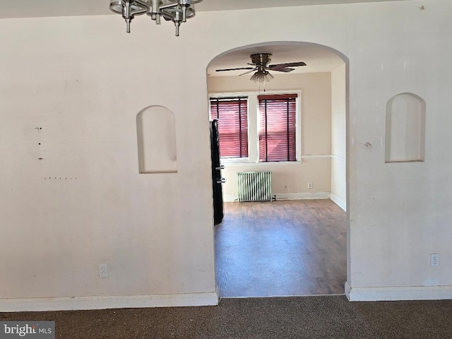 empty room featuring arched walkways, radiator, baseboards, and ceiling fan