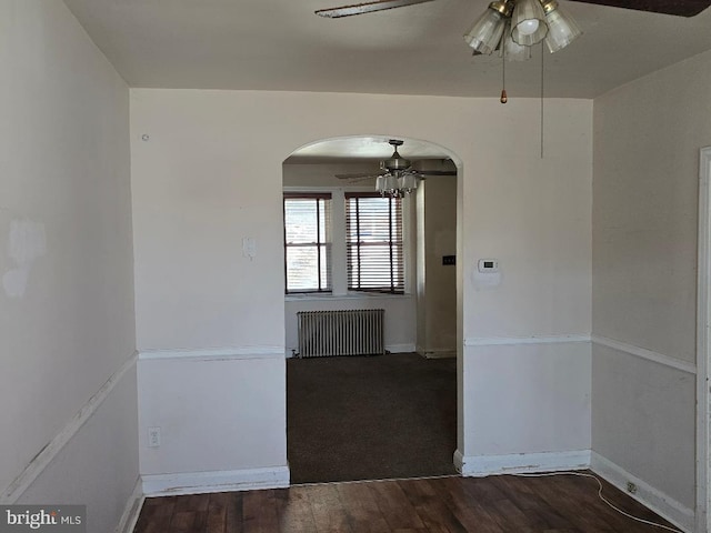 spare room with a ceiling fan, wood finished floors, radiator heating unit, arched walkways, and baseboards