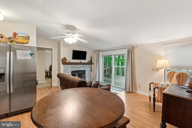 dining area featuring a ceiling fan, baseboards, lofted ceiling, light wood-style flooring, and a stone fireplace