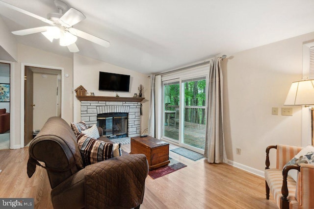 living area featuring a stone fireplace, baseboards, light wood-type flooring, and lofted ceiling