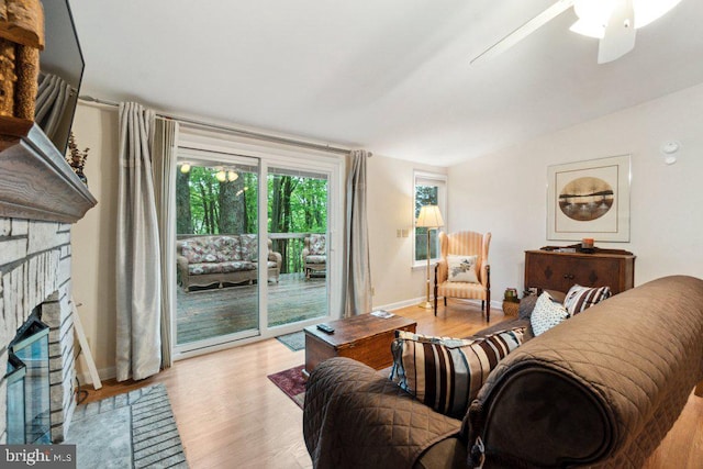 living area with baseboards, a brick fireplace, ceiling fan, and light wood finished floors