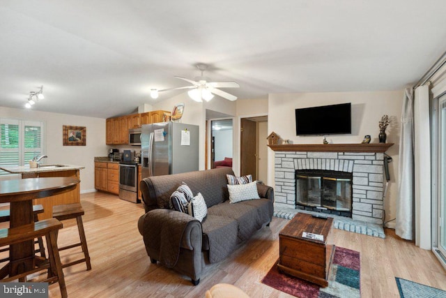 living area featuring a stone fireplace, vaulted ceiling, a ceiling fan, and light wood finished floors