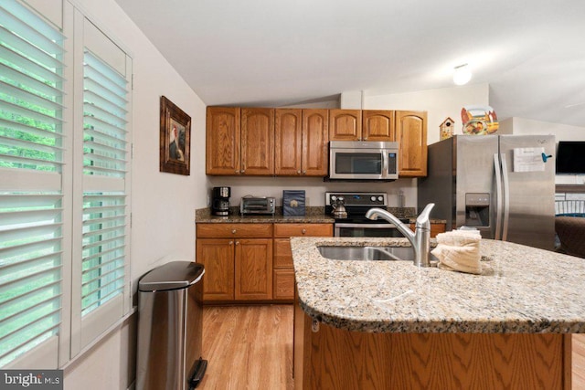 kitchen featuring light stone countertops, brown cabinets, a sink, stainless steel appliances, and light wood-type flooring