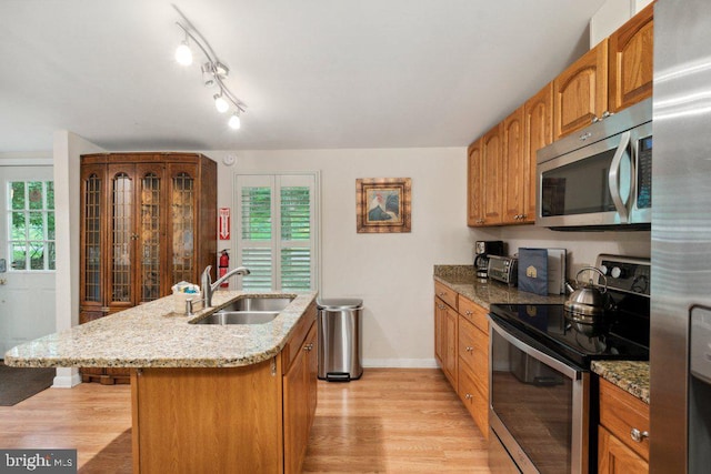 kitchen with light stone counters, an island with sink, a sink, stainless steel appliances, and light wood-style floors