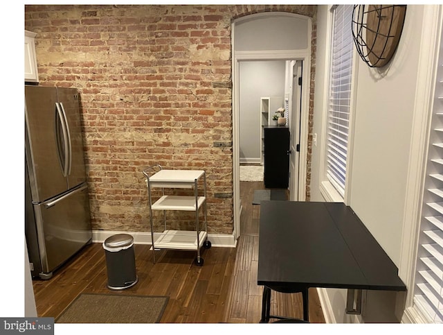 kitchen with dark wood-type flooring, freestanding refrigerator, brick wall, white cabinets, and baseboards