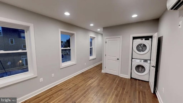 clothes washing area with an AC wall unit, wood finished floors, stacked washing maching and dryer, baseboards, and laundry area