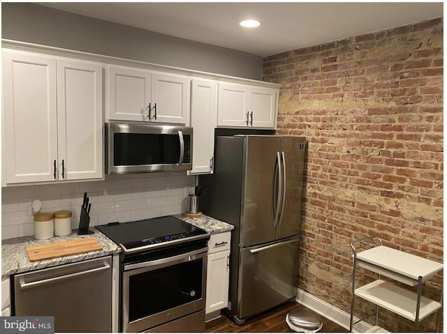 kitchen featuring dark wood-type flooring, backsplash, white cabinetry, stainless steel appliances, and brick wall