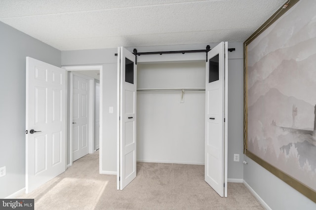 unfurnished bedroom with a barn door, light carpet, baseboards, and a closet