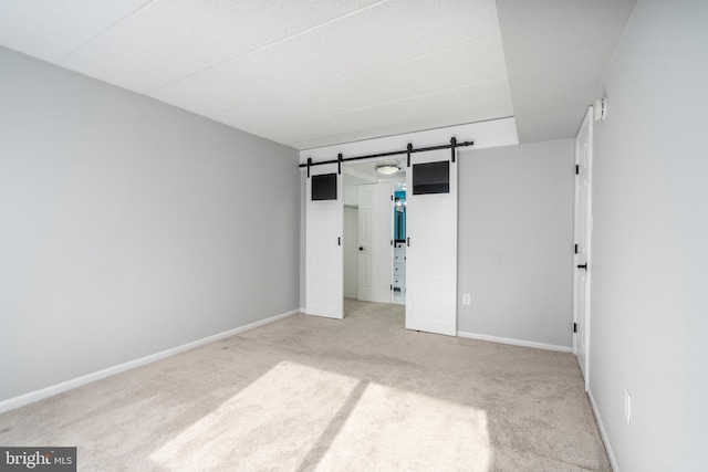 unfurnished bedroom featuring baseboards, carpet, and a barn door