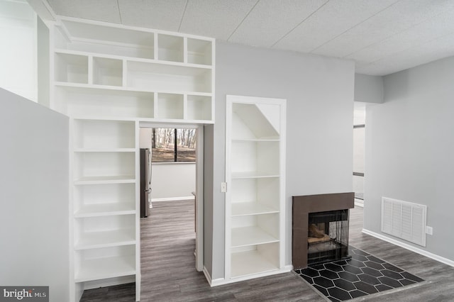 unfurnished living room with a multi sided fireplace, visible vents, baseboards, and dark wood-style flooring