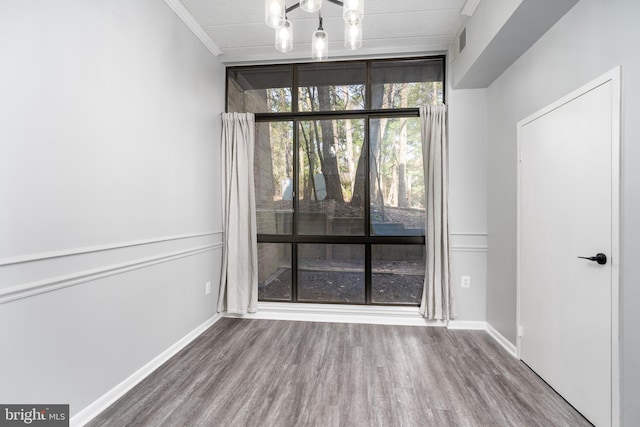 empty room with visible vents, crown molding, baseboards, wood finished floors, and a notable chandelier