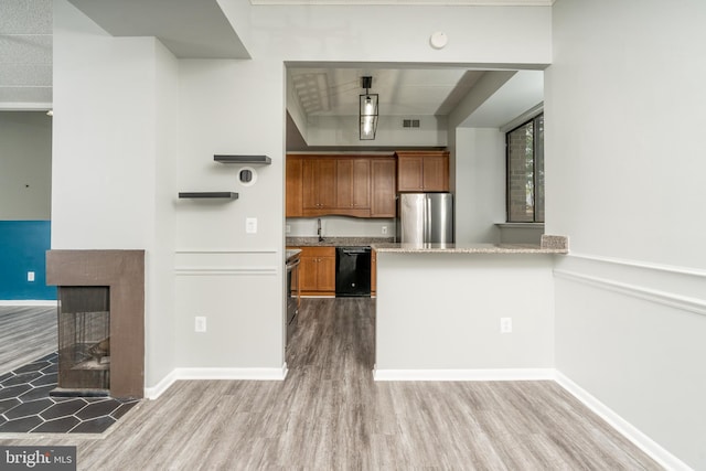 kitchen featuring brown cabinetry, wood finished floors, a multi sided fireplace, and appliances with stainless steel finishes