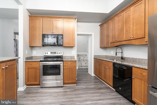 kitchen with light stone countertops, brown cabinets, wood finished floors, black appliances, and a sink