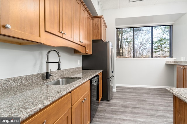 kitchen with a sink, black dishwasher, light wood finished floors, baseboards, and light stone countertops