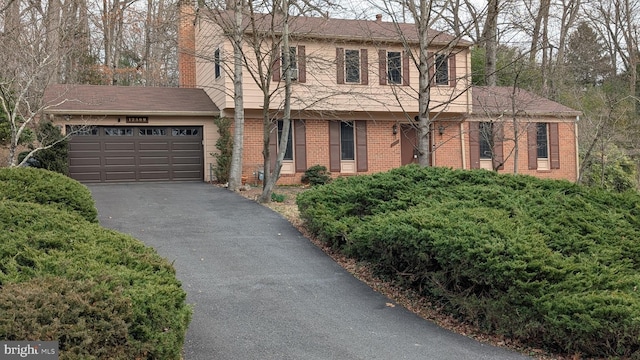 colonial home featuring aphalt driveway, an attached garage, brick siding, and a chimney