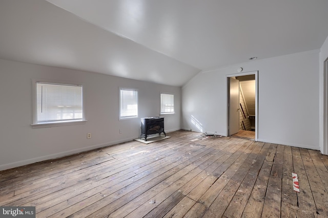 unfurnished living room featuring baseboards, lofted ceiling, hardwood / wood-style floors, and a wood stove