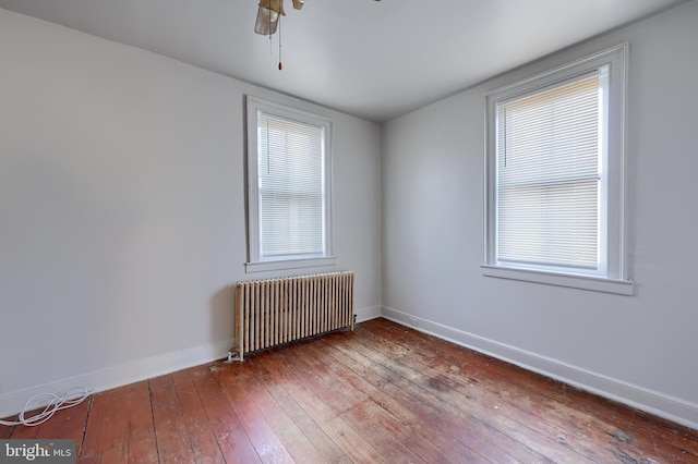 spare room featuring baseboards, radiator, a ceiling fan, and hardwood / wood-style flooring