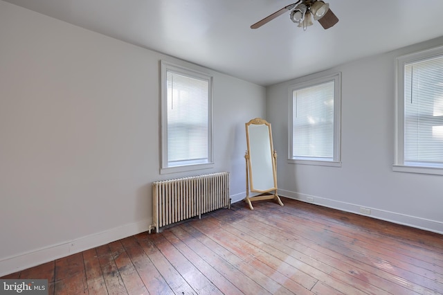 empty room with hardwood / wood-style flooring, radiator heating unit, a ceiling fan, and baseboards