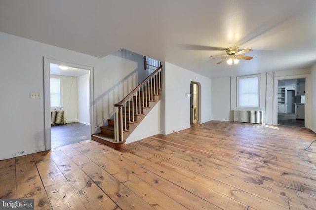 interior space with arched walkways, stairs, radiator heating unit, and hardwood / wood-style floors