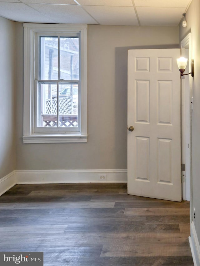 spare room featuring dark wood finished floors, a drop ceiling, and baseboards