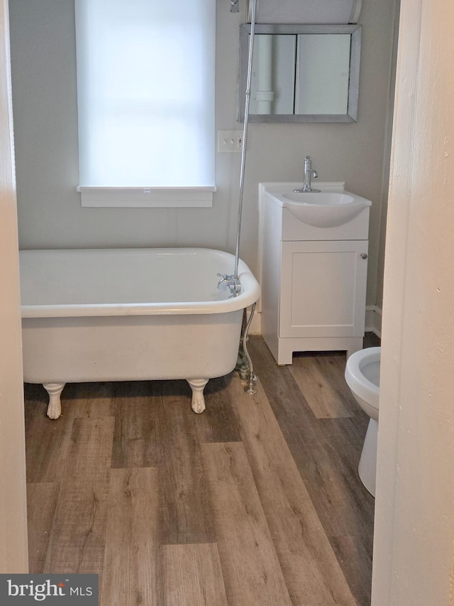 full bath with a freestanding bath, wood finished floors, vanity, and toilet