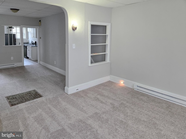 empty room featuring visible vents, arched walkways, light colored carpet, and a baseboard heating unit