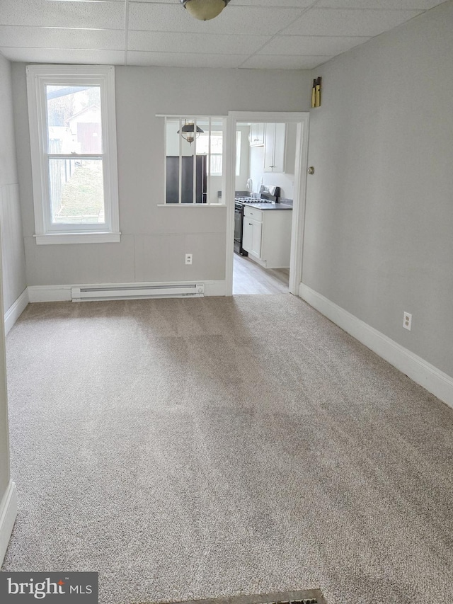 unfurnished living room featuring a paneled ceiling, a baseboard radiator, light carpet, and baseboards