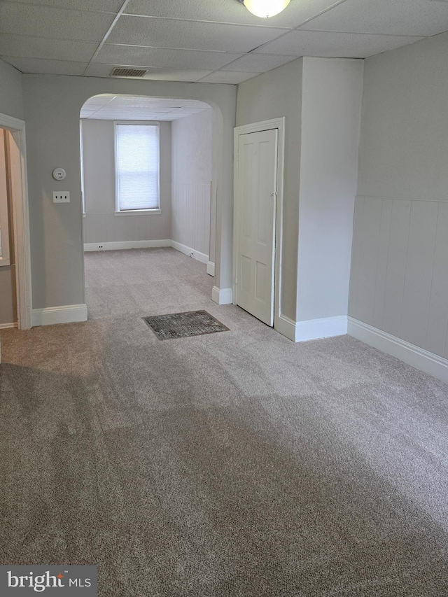 carpeted spare room featuring arched walkways, a drop ceiling, and visible vents