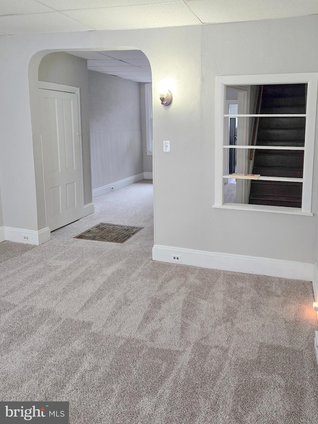 unfurnished room featuring baseboards, a drop ceiling, carpet floors, wainscoting, and arched walkways