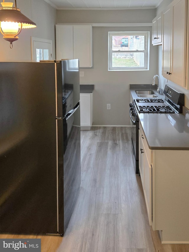 kitchen featuring freestanding refrigerator, light wood-style flooring, range with gas cooktop, and a sink