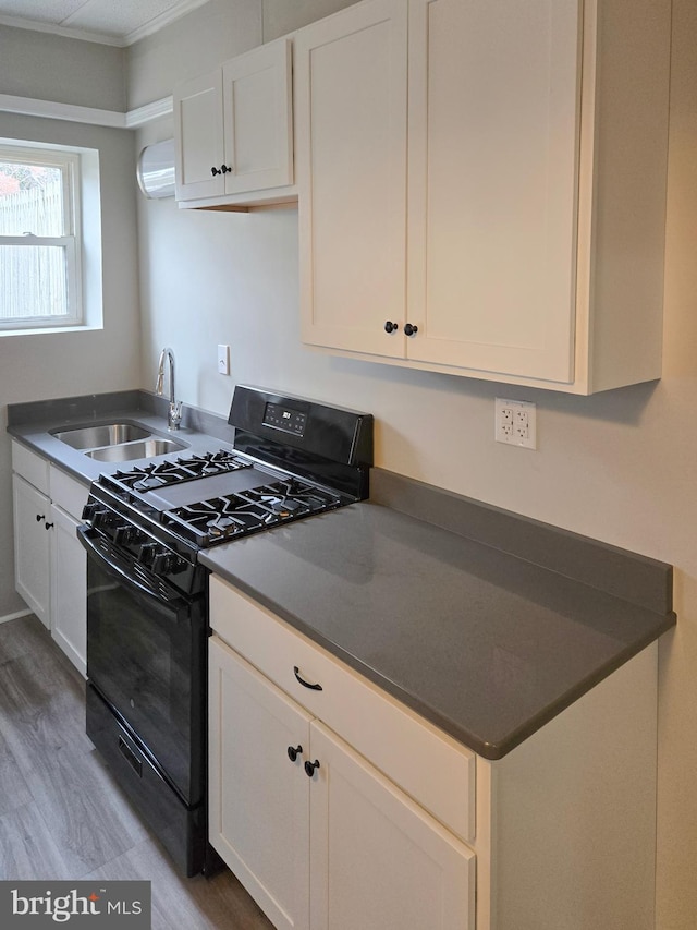 kitchen with a sink, light wood-style floors, dark countertops, and black gas stove