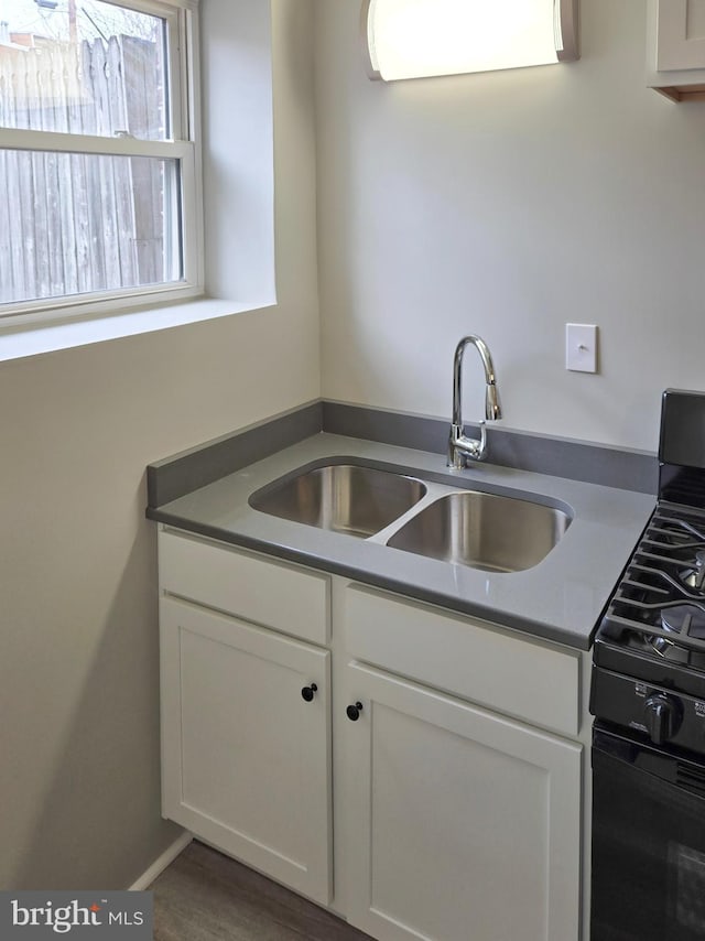 kitchen featuring black gas stove, white cabinetry, and a sink