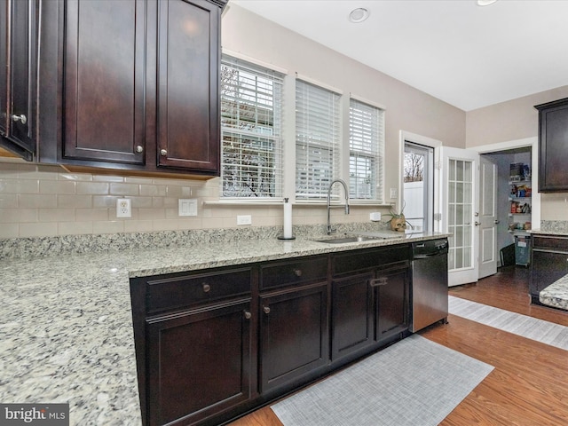 kitchen with a sink, backsplash, stainless steel dishwasher, dark brown cabinetry, and light wood finished floors