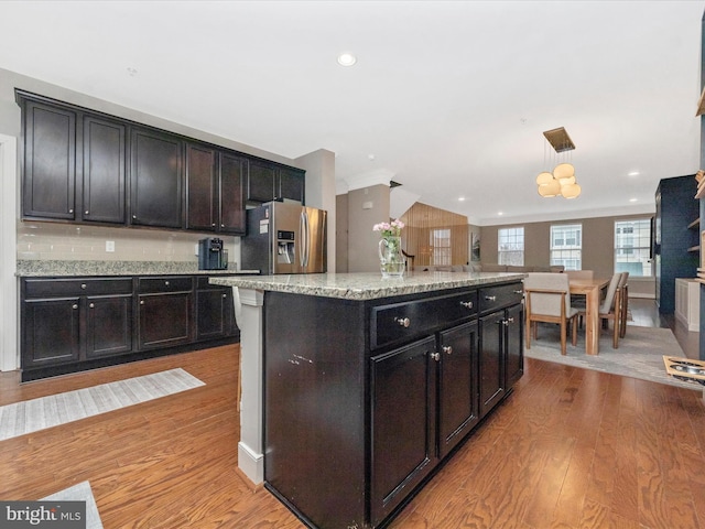 kitchen with light wood-style flooring, decorative light fixtures, light stone counters, a center island, and stainless steel fridge