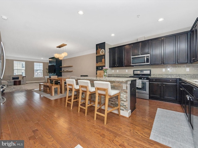 kitchen with light stone countertops, open floor plan, a kitchen bar, wood finished floors, and stainless steel appliances