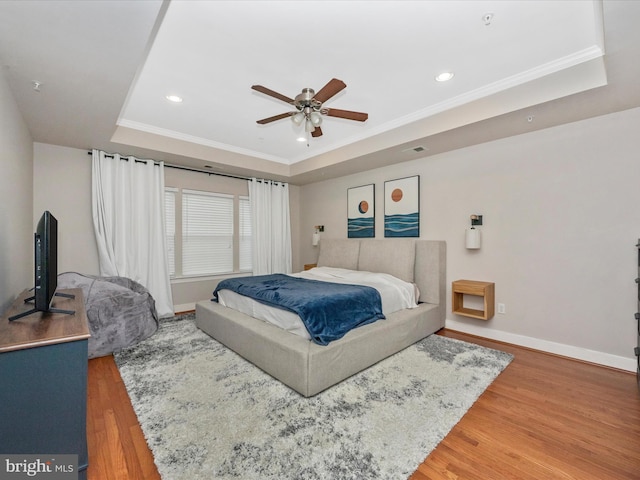 bedroom featuring a raised ceiling, baseboards, light wood-type flooring, and ornamental molding