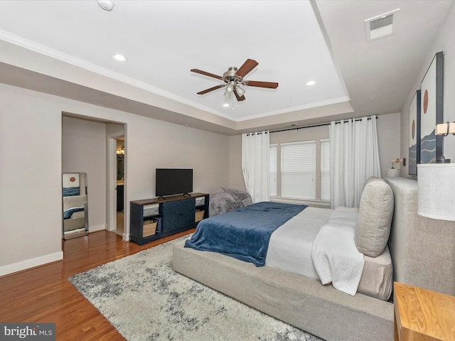 bedroom with visible vents, wood finished floors, baseboards, crown molding, and a raised ceiling