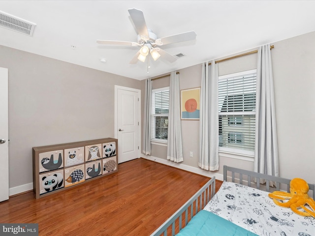 bedroom with a ceiling fan, wood finished floors, visible vents, and baseboards