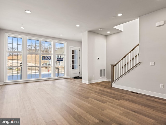 unfurnished living room featuring a wealth of natural light, visible vents, wood finished floors, and stairway