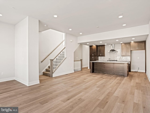 kitchen featuring wall chimney range hood, tasteful backsplash, recessed lighting, light wood finished floors, and light countertops