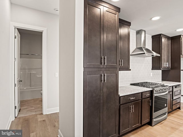 kitchen with backsplash, dark brown cabinetry, stainless steel range with gas stovetop, light wood-type flooring, and wall chimney exhaust hood