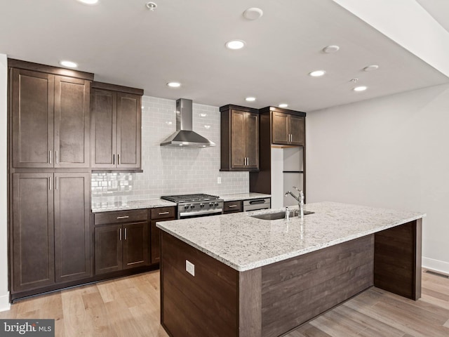 kitchen with light wood finished floors, a sink, decorative backsplash, stainless steel stove, and wall chimney exhaust hood