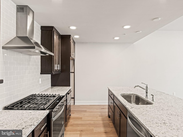 kitchen featuring a sink, light wood-style floors, appliances with stainless steel finishes, wall chimney range hood, and dark brown cabinets