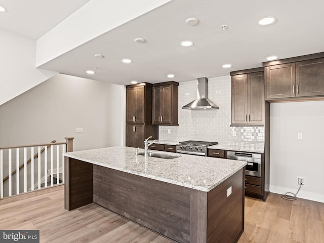 kitchen with a sink, dark brown cabinets, appliances with stainless steel finishes, wall chimney exhaust hood, and light wood-type flooring