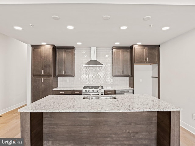 kitchen with dark brown cabinets, wall chimney range hood, light wood-type flooring, decorative backsplash, and a sink