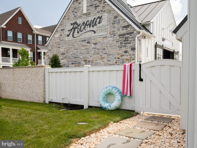 exterior space with a gate, fence, stone siding, a lawn, and board and batten siding