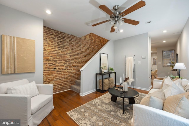 living area with stairway, a ceiling fan, baseboards, brick wall, and hardwood / wood-style flooring