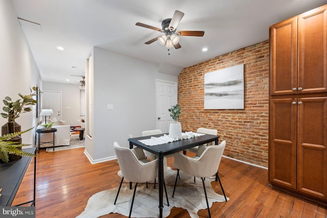 dining room with hardwood / wood-style floors, a ceiling fan, and brick wall