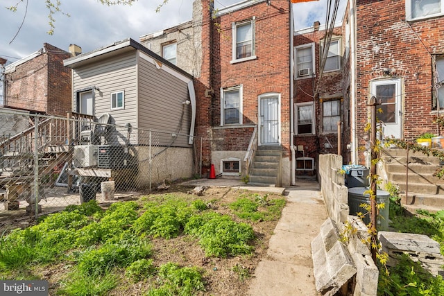 rear view of property with brick siding, entry steps, and fence